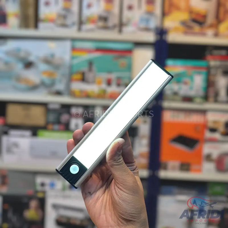 A hand holding a sleek, silver LED light bar with a circular button on one end.