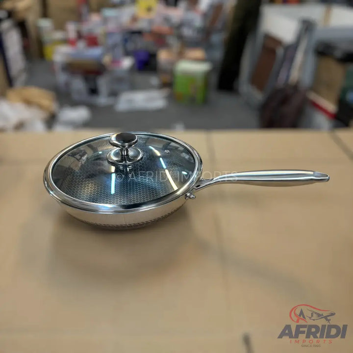 A stainless steel frying pan with a glass lid and a honeycomb non-stick interior.