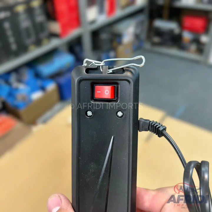 Black handheld device with a red rocker switch and power cord.