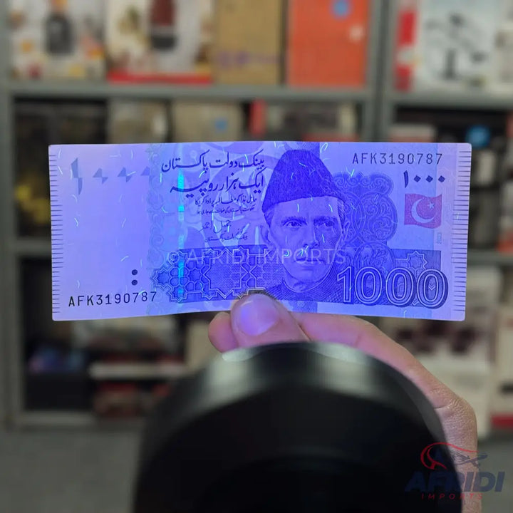 A counterfeit Pakistani 1000 rupee note illuminated by UV light.