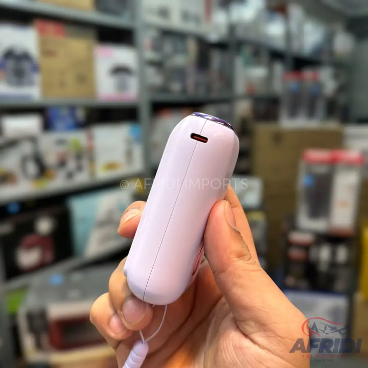 A person’s hand holding a light purple, smooth, cylindrical electronic device with a dark, reflective top and a small red light in a slot.