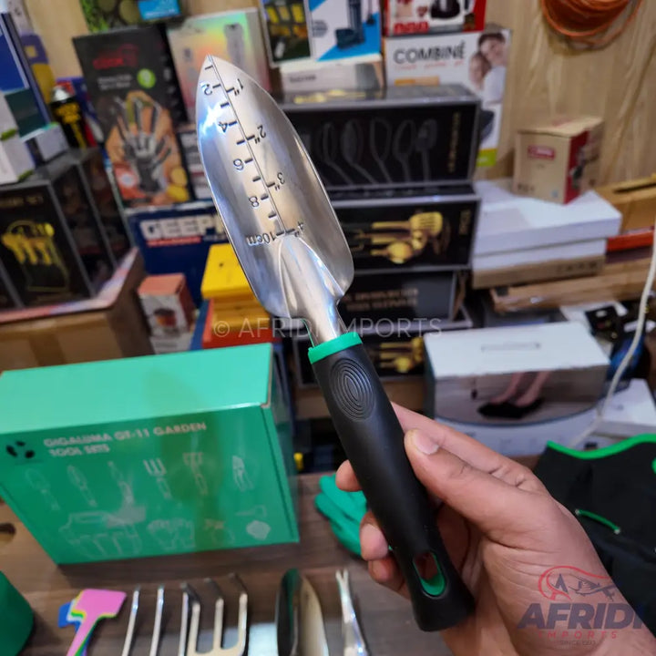 A hand trowel with a black and green ergonomic handle and a silver blade marked with depth measurements in inches and centimeters.