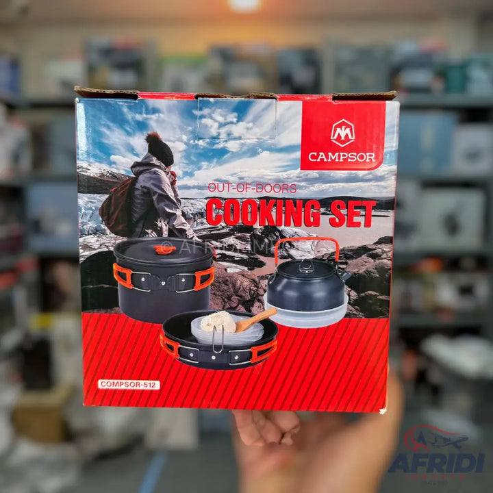A boxed outdoor cooking set featuring a pot, kettle, and frying pan with orange accents, designed for camping.