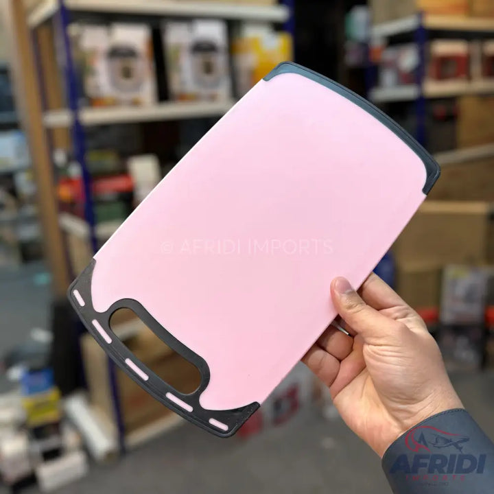 Pink plastic cutting board with a black non-slip edge and integrated handle.
