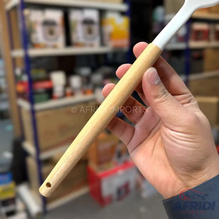 A cooking spatula with a light wooden handle and a white silicone head.