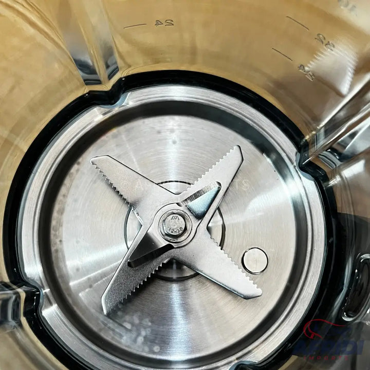 A stainless steel blender blade with serrated edges, mounted inside a clear container.