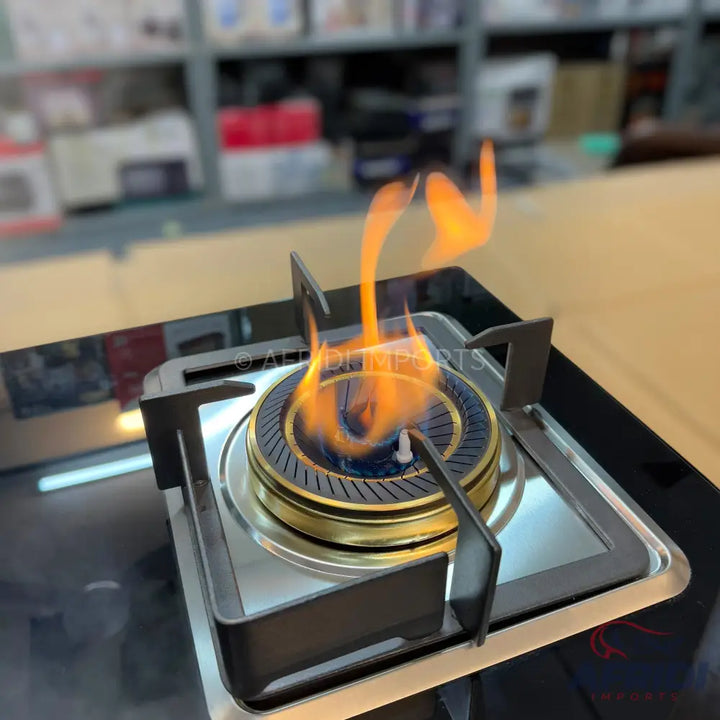 A single burner gas stove with a black glass top and a blue and gold burner, featuring an active flame.