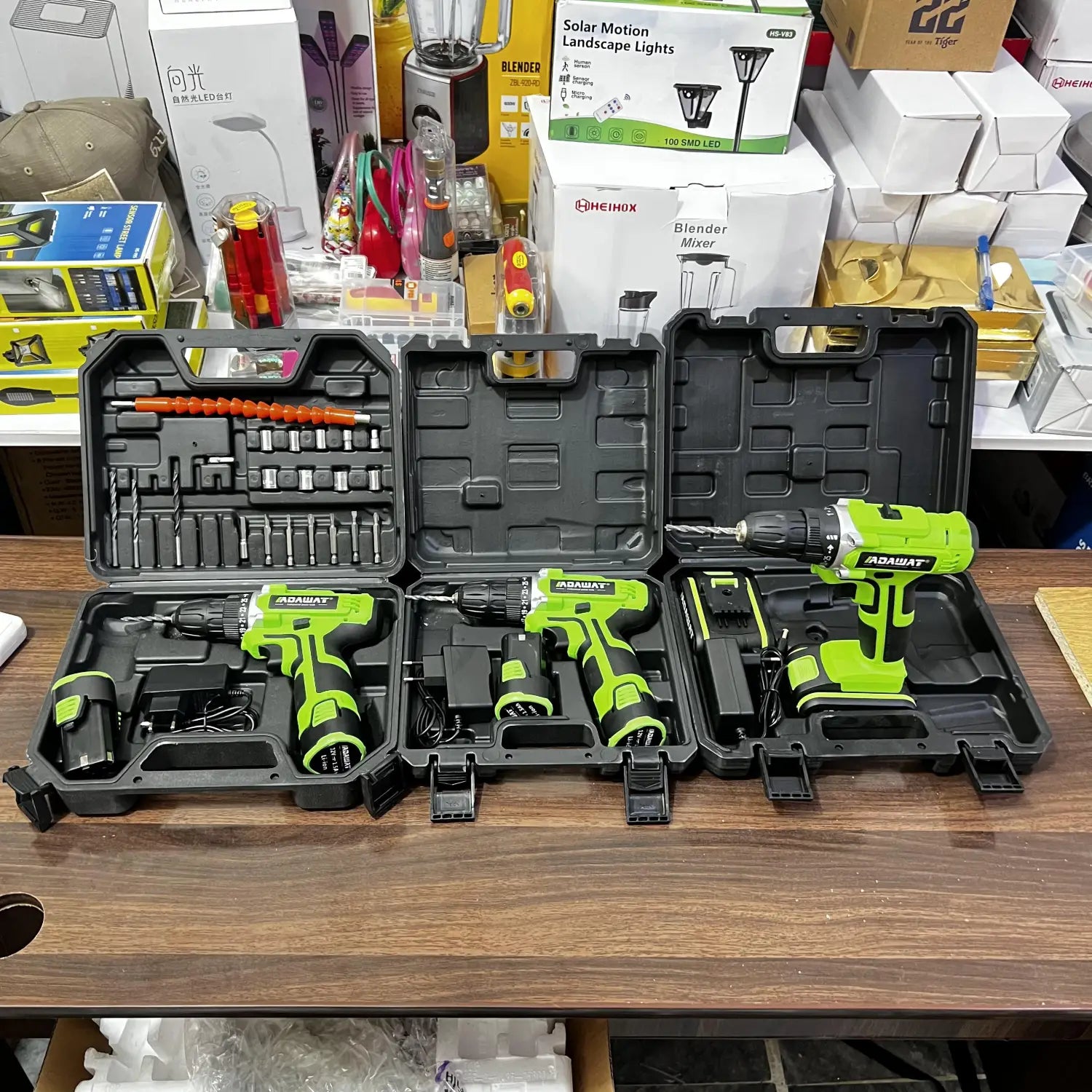 Three green and black cordless drills in open cases with accessories, part of the Lot Imported Adawat Portable Rechargeable Drill Set featuring a volt drill set and battery backup with hard case included