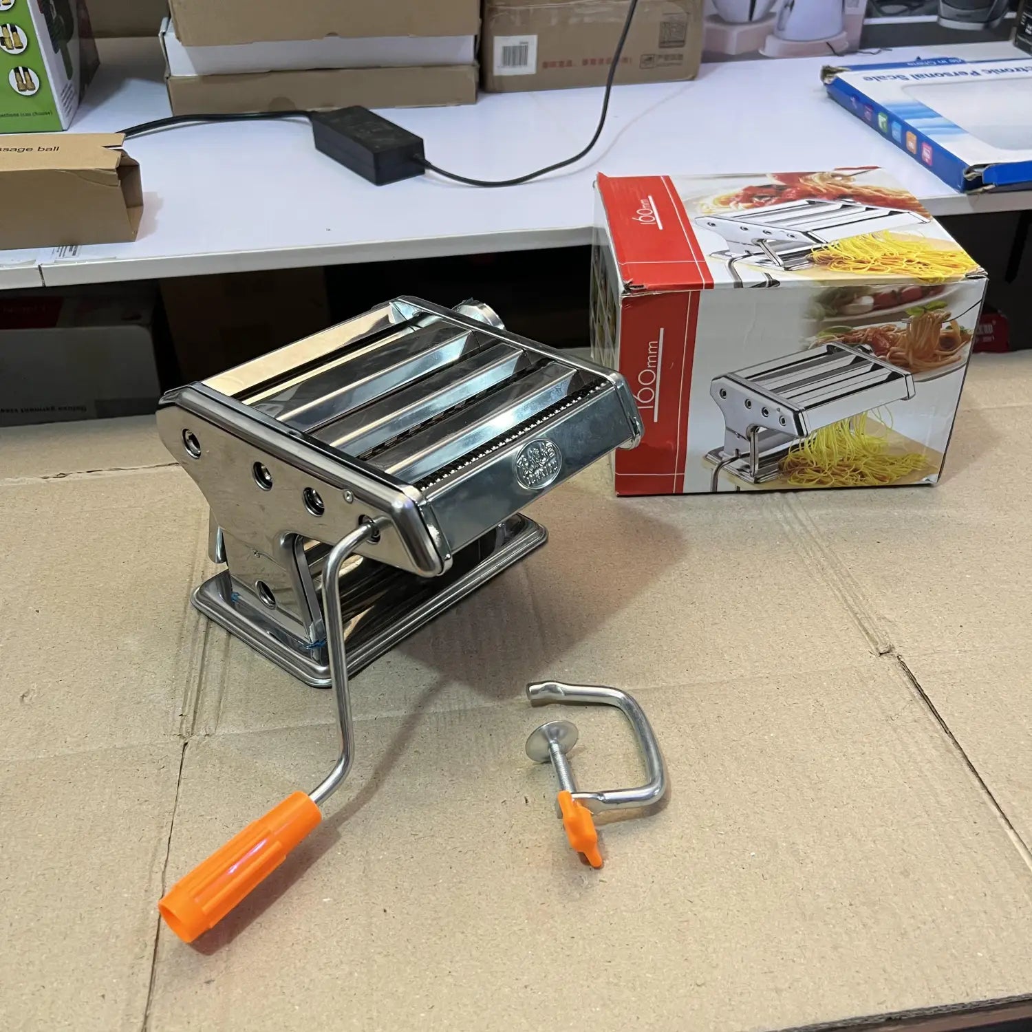 Silver manual pasta maker with orange handle and clamp for homemade pasta preparation