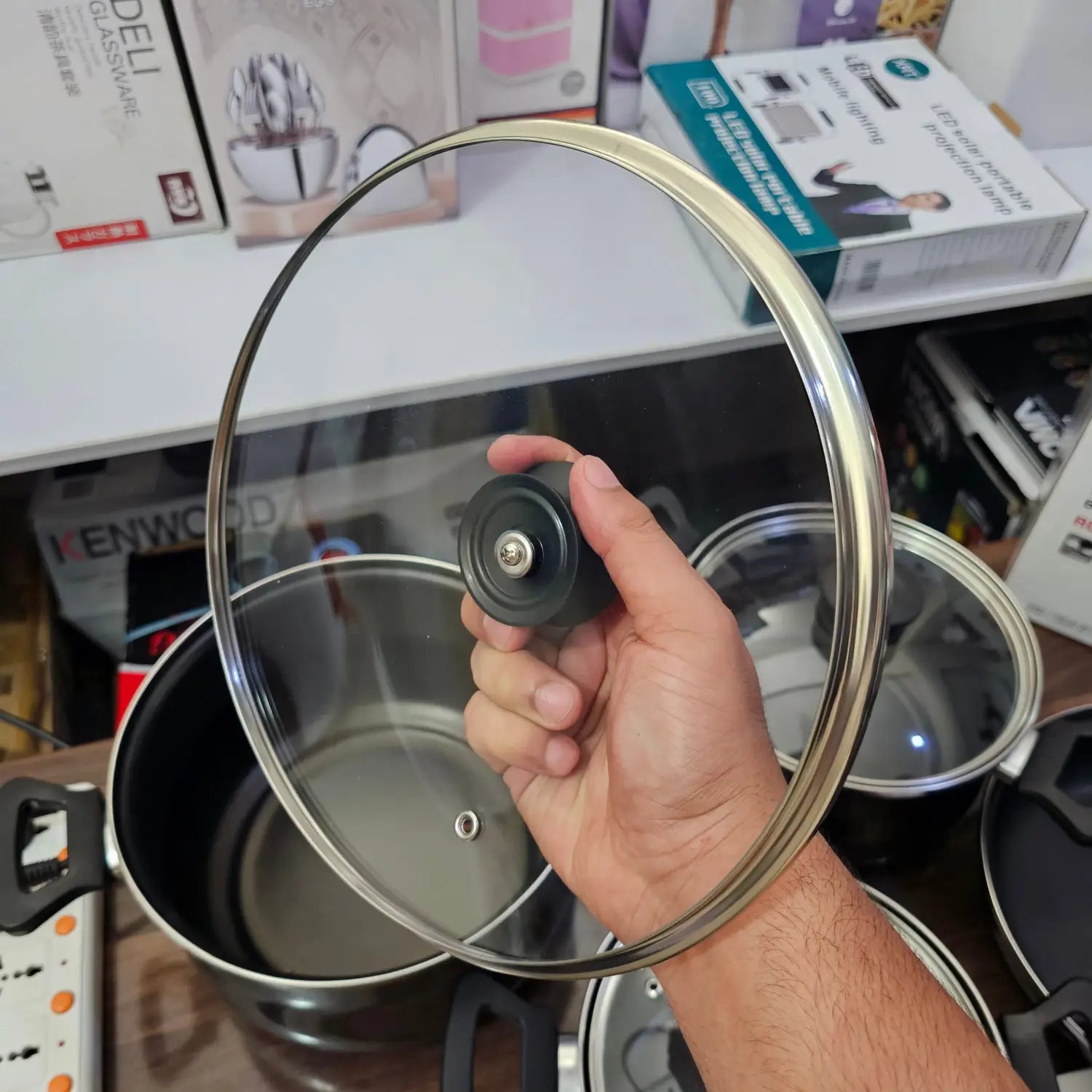 Hand holding a clear glass pot lid with black knob from German Lot Imported Megafesa cookware set