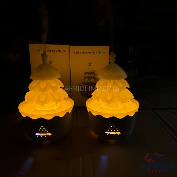 Two glowing Christmas tree-shaped aroma diffusers with decorative bases.