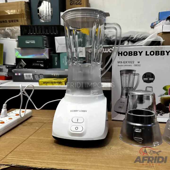 A white blender with a clear pitcher and two control buttons, accompanied by a smaller clear grinding attachment.
