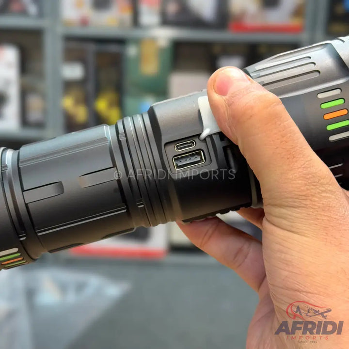 A black, cylindrical flashlight with multiple charging ports, including USB-A and USB-C, and a battery indicator on its side.