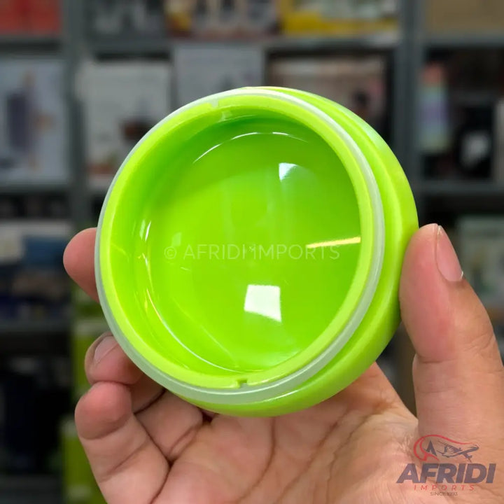 A bright green, round, plastic container with a clear, domed lid, held in a hand.