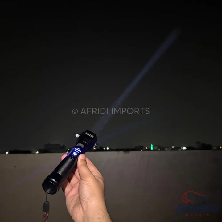 A black handheld flashlight with a blue light beam projecting into the night sky.