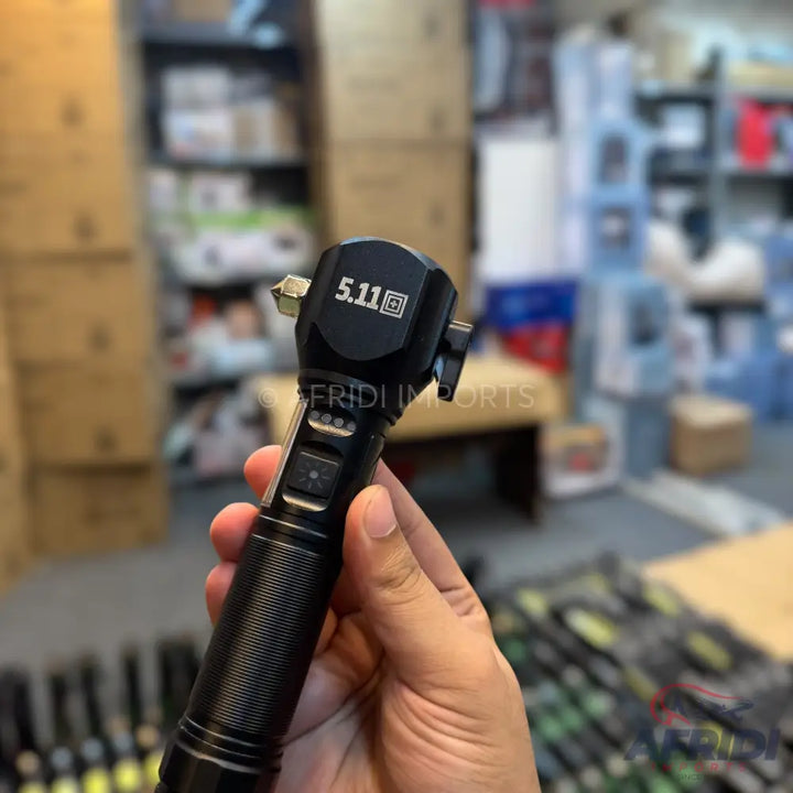 Black 5.11 tactical flashlight with a glass breaker and seatbelt cutter, held in a hand.