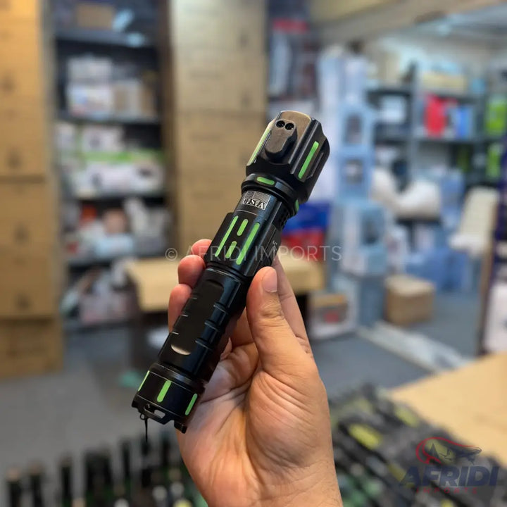A black flashlight with green glowing accents, held in a hand.