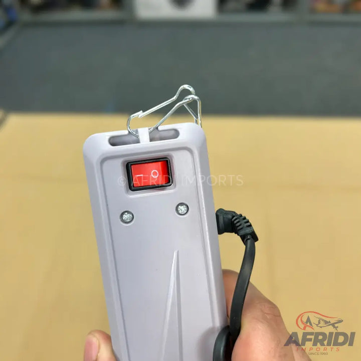 A handheld electronic device with a red on/off switch, two indicator lights, a metal loop, and a power cord.