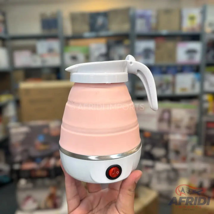 A pink and white collapsible electric travel kettle with a folding handle and an on/off switch.