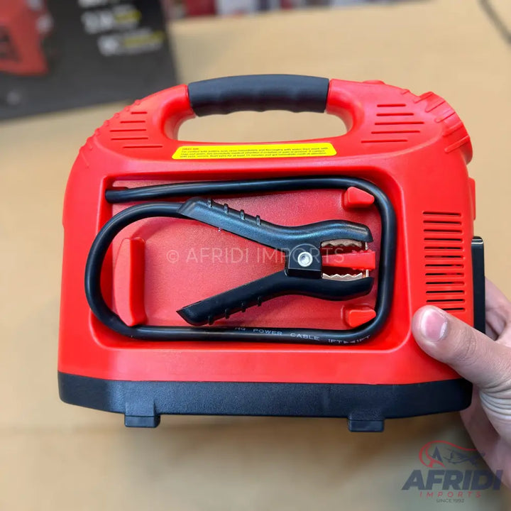 Red portable car jump starter with attached jumper cables.