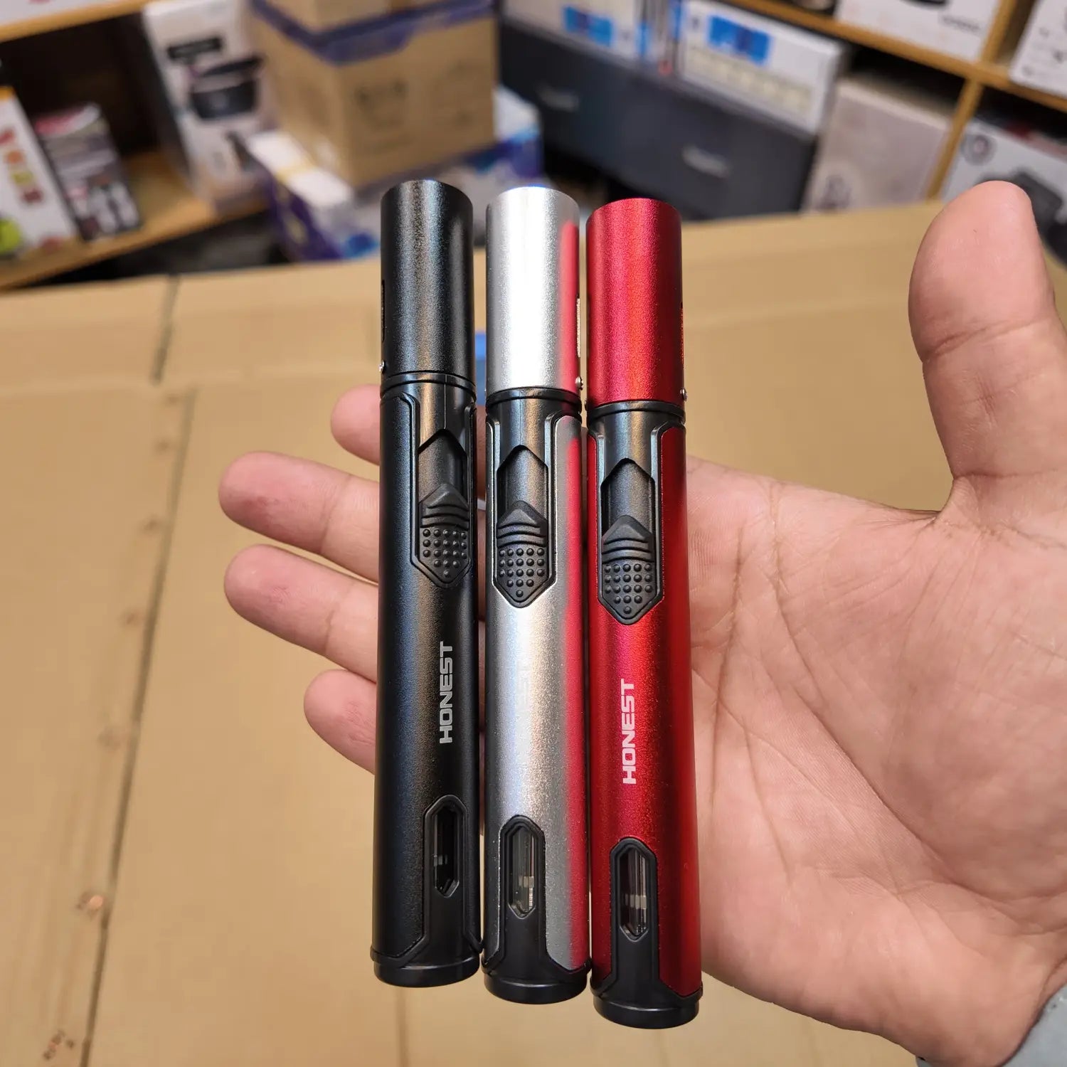 Hand holding three slim jet flame lighters in black, silver, and red for Lot Imported Honest Jet Flame Lighter