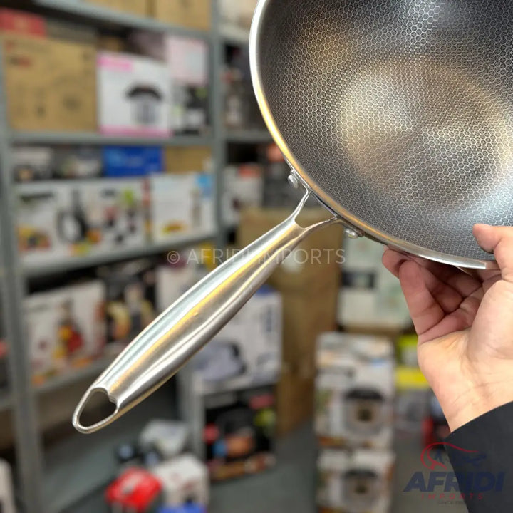 Stainless steel wok with a honeycomb texture and a sturdy handle.