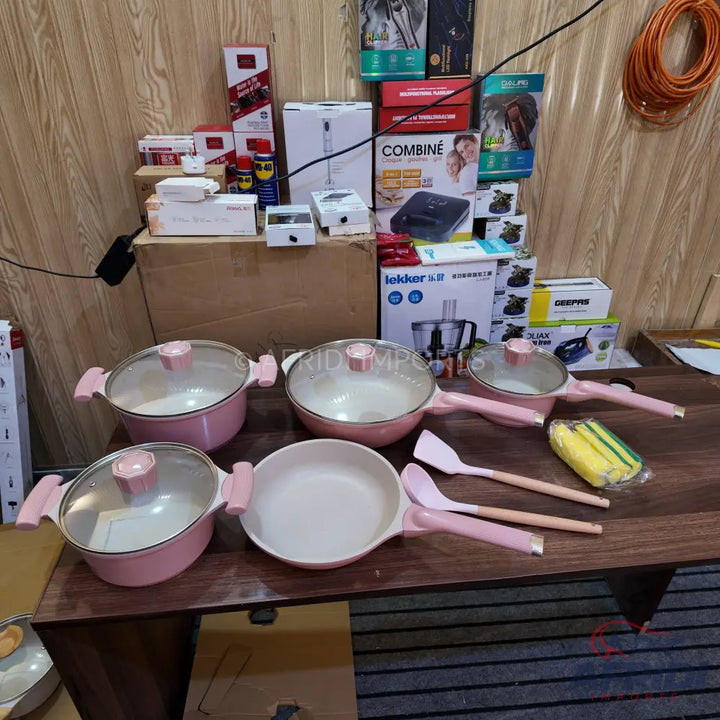 A set of pink cooking pots and pans with clear lids and matching utensils.