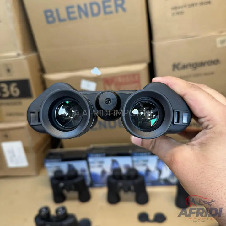 Black binoculars with green-coated lenses held in a hand.
