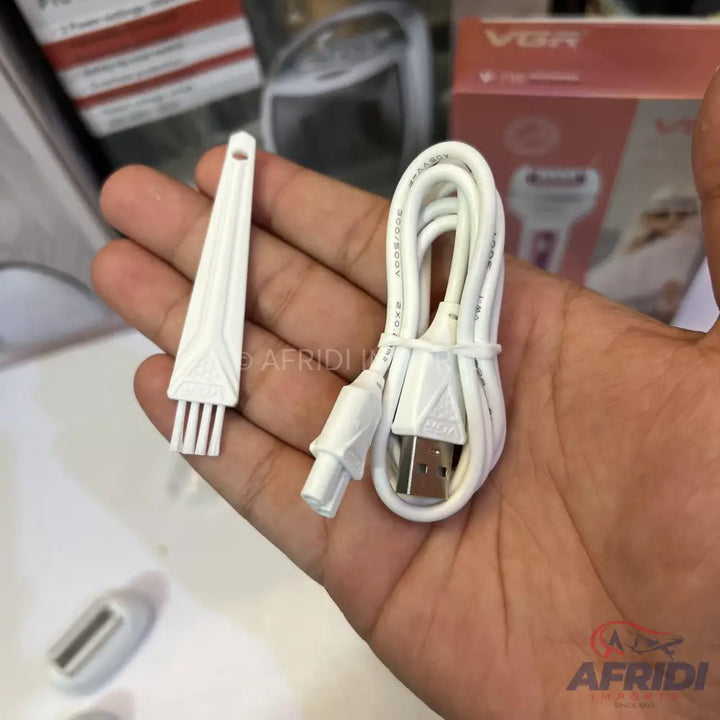 A white cleaning brush and a coiled USB charging cable with a barrel connector.