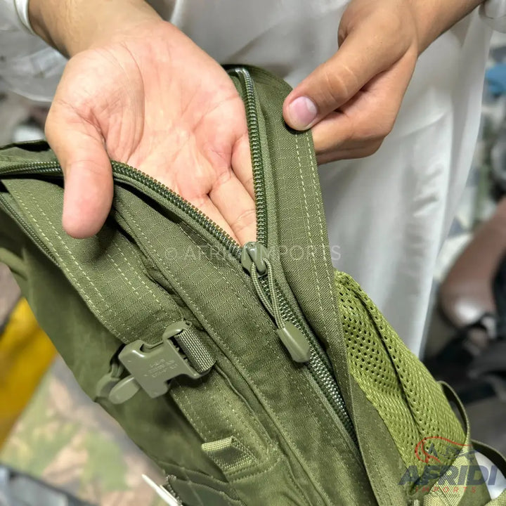 A person’s hands opening a green tactical backpack with a zipper closure and a side buckle.