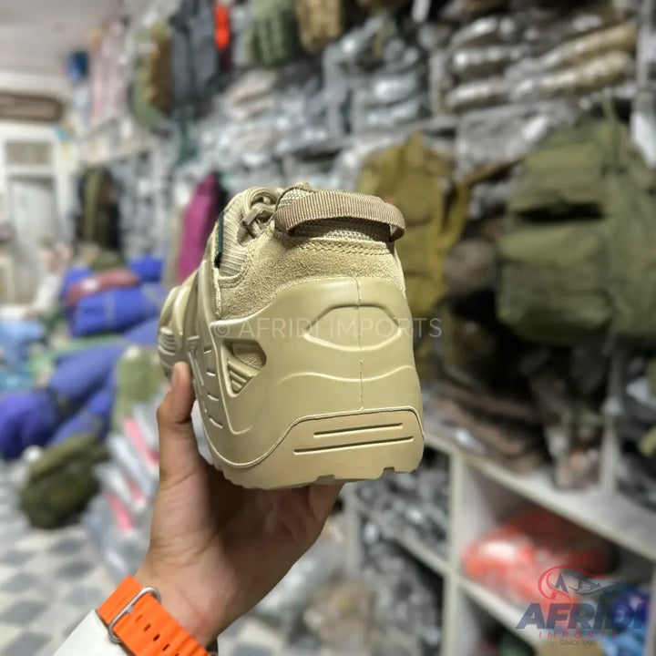A single, tan-colored outdoor or tactical shoe.