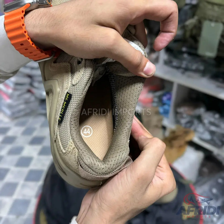 A person’s hands holding a tan sneaker, revealing the inside with a size 44 marking.