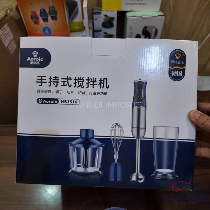 A white box containing a handheld immersion blender with various attachments including a chopper, whisk, and measuring cup.