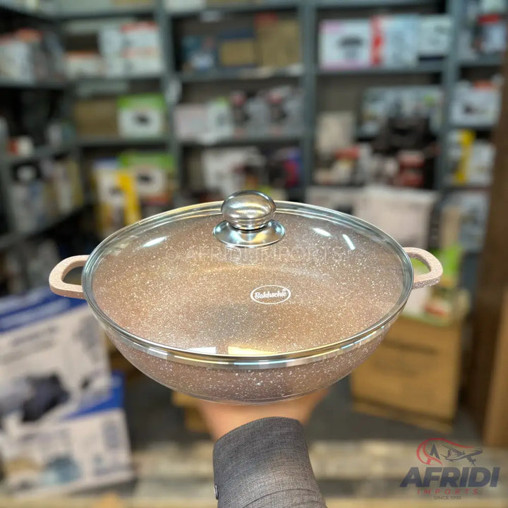 A speckled, round cooking pot with a glass lid and two handles.