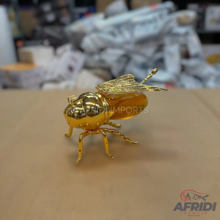 A novelty golden bee-shaped container filled with honey and a golden dipper.