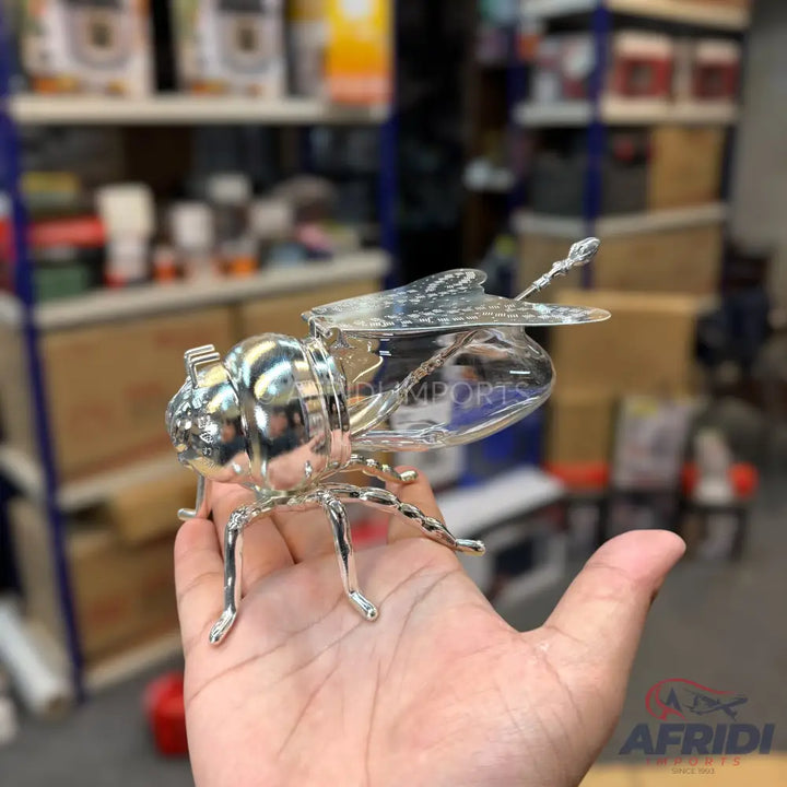 A shiny, silver-colored metal insect-shaped tea infuser with an opening lid.