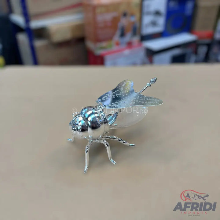 A silver-plated insect figurine with textured wings and a segmented body.