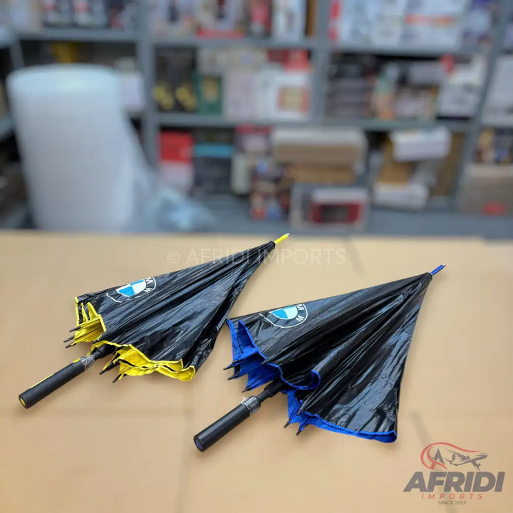 Two black umbrellas with BMW logos and colored undersides, one yellow and one blue.