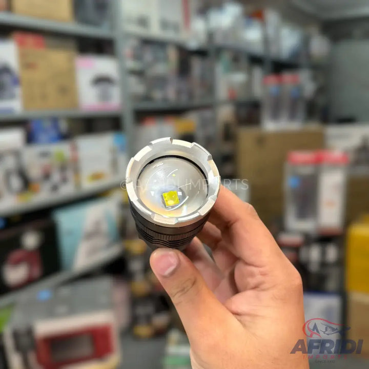 A silver and black flashlight with a bright yellow LED bulb.