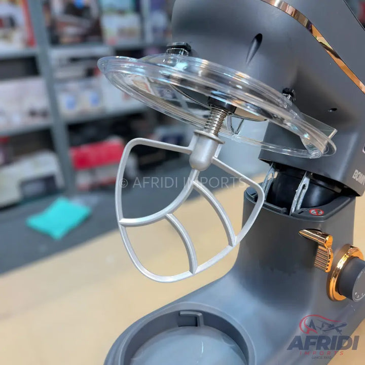 A dark grey stand mixer with gold accents, a clear splash guard, and a paddle attachment.