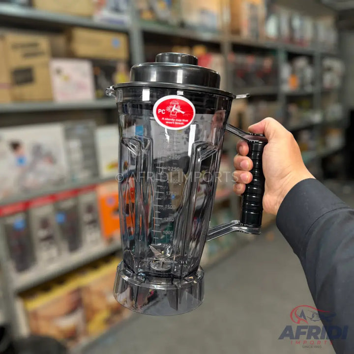 A clear plastic blender pitcher with a black lid and handle, featuring measurement markings.