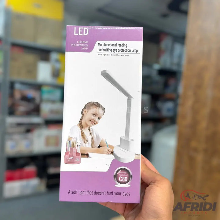 A white, foldable LED desk lamp with a built-in pen holder, designed for eye protection during reading and writing.
