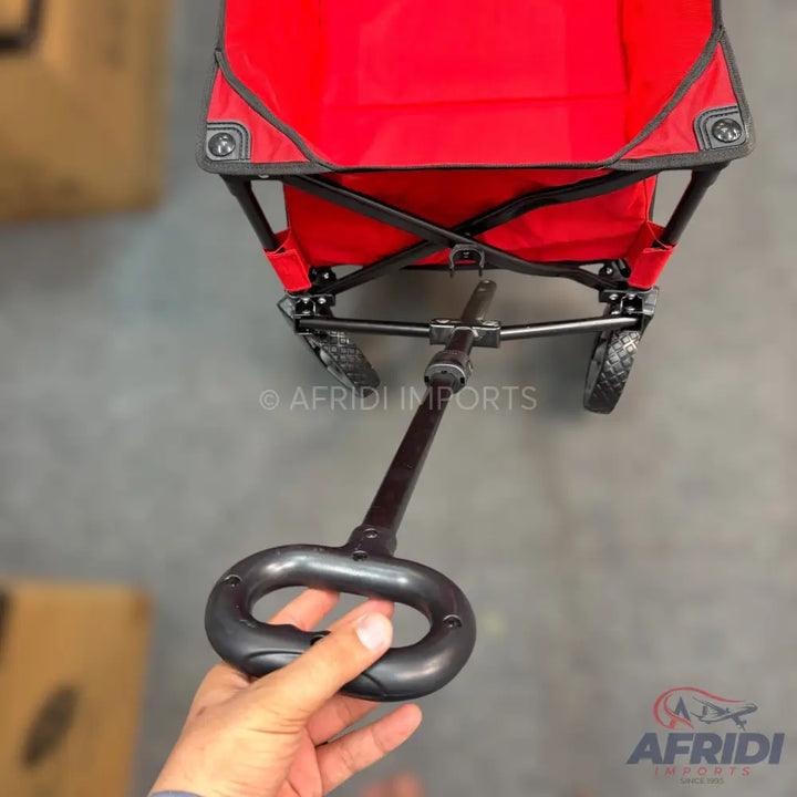 Red fabric folding wagon with a black handle and wheels.