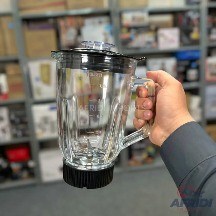Clear glass blender jar with a black lid and base, held by a hand.