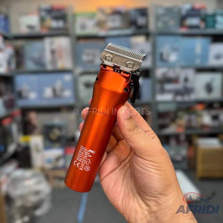 An orange-metallic electric hair clipper with a silver blade, featuring a lever for adjusting the cutting length.