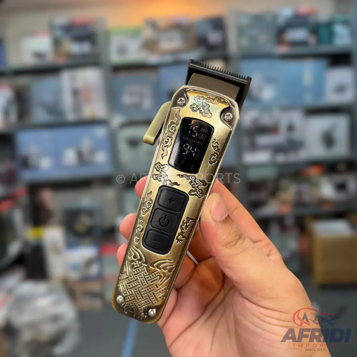 Gold-colored hair clipper with an intricate engraved design, digital display, and three control buttons.