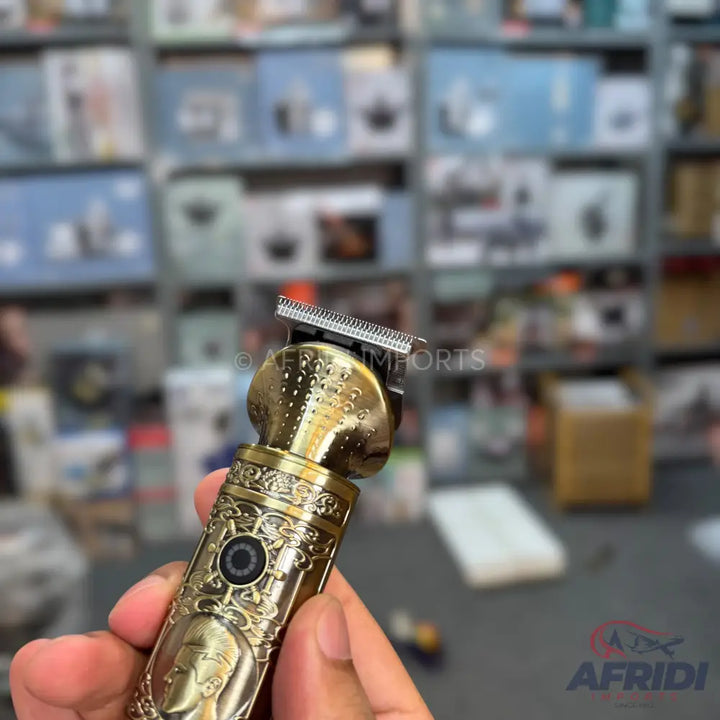 A gold-colored, intricately carved electric hair trimmer with a visible on/off button and a detailed blade head.