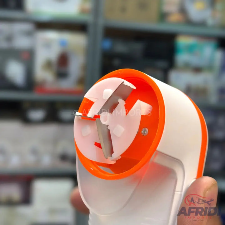 A handheld white and orange garlic press or vegetable dicer with an exposed blade.
