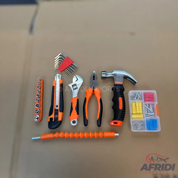 An assortment of hand tools with orange and black handles, including a hammer, pliers, adjustable wrench, utility knife, socket set, hex key set, flexible bit extension, and a box of screws and wall anchors.