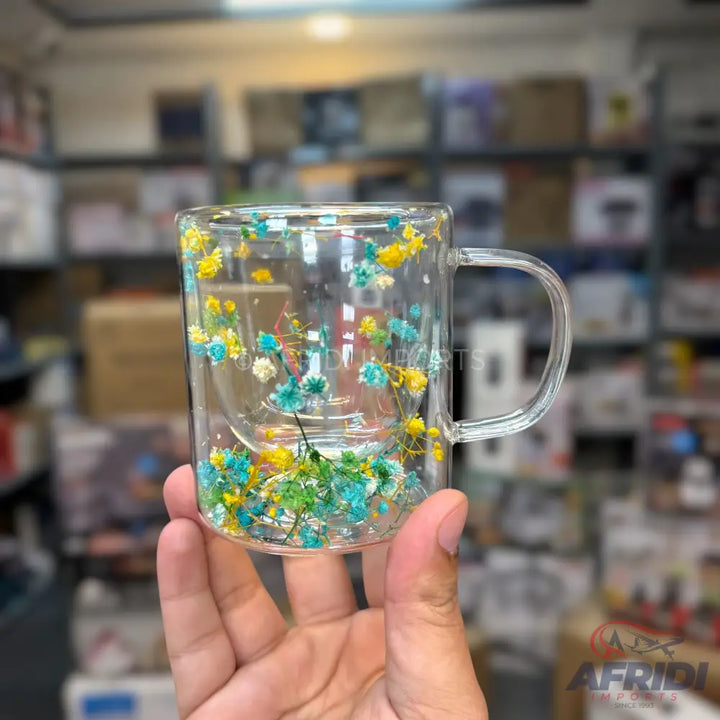 A clear glass double-walled mug with a handle, containing colorful dried flowers in its outer wall.